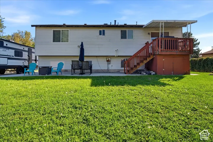 Rear exterior featuring a wood deck with stairs, a patio area, and a grass lawn
