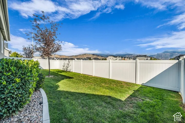 Fenced backyard featuring a manicured lawn, established tree, and shrubbery