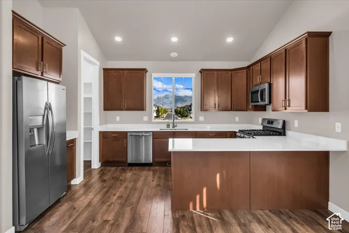 Kitchen featuring wood-finish flooring, stainless steel appliances, white countertops, dark wood cabinetry, and recessed lighting