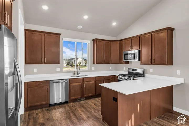 Kitchen featuring wood-finish flooring, stainless steel appliances, white countertops, rich wood cabinetry, and vaulted ceilings