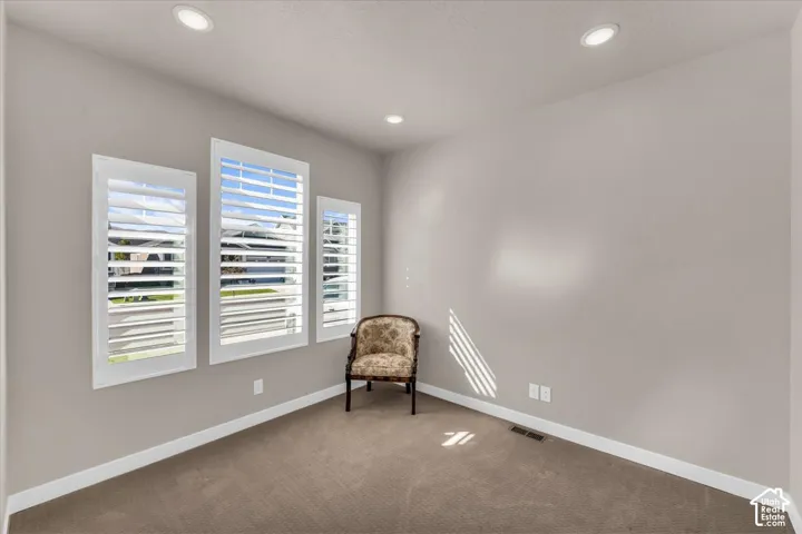 Recessed lighting, three windows with white plantation shutters, neutral wall tones, and carpeted flooring