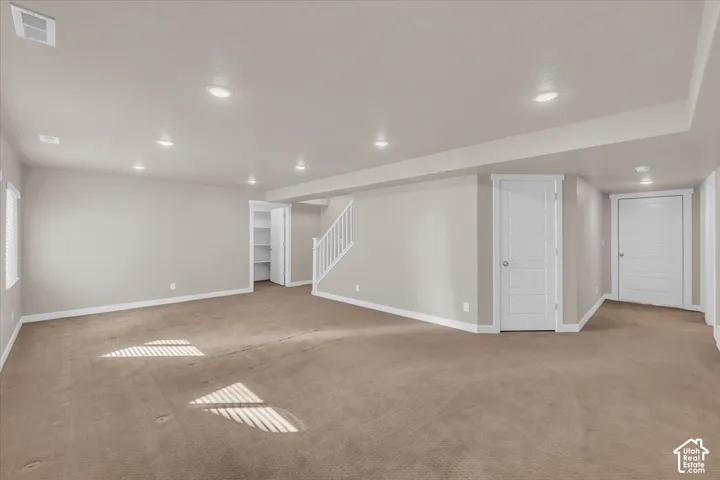 Expansive carpeted area featuring recessed lighting, a white staircase, and built-in shelving
