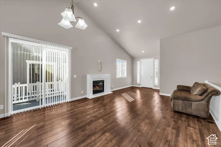 Vaulted ceiling with recessed lighting, wood-finish flooring, white fireplace with mantle, sliding glass door, and white plantation shutters