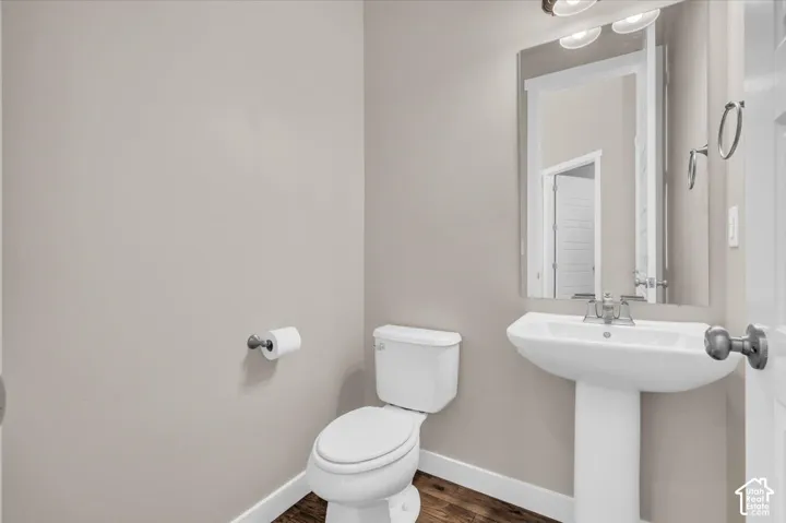 Pedestal sink, wall-mounted mirror, two-bulb vanity light, and dark wood-finish flooring