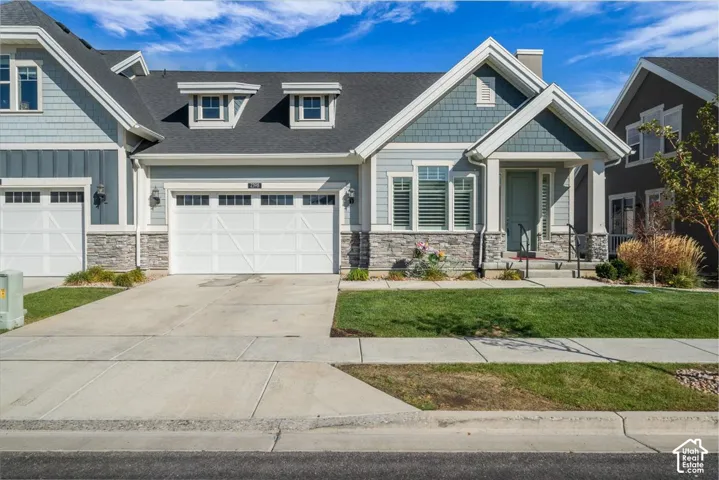 Exterior featuring a covered entryway, dual garage doors, decorative stone accents, and a well-maintained lawn