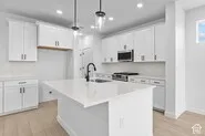 Kitchen featuring white cabinetry, a central island with a sink, stainless steel appliances, a tile backsplash, and wood-finish flooring