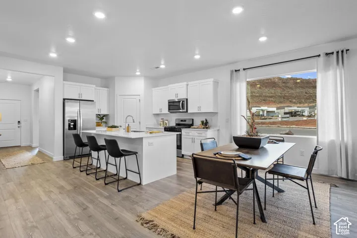 Bright open-concept kitchen and dining area featuring white cabinetry, stainless steel appliances, and a central island with counter seating