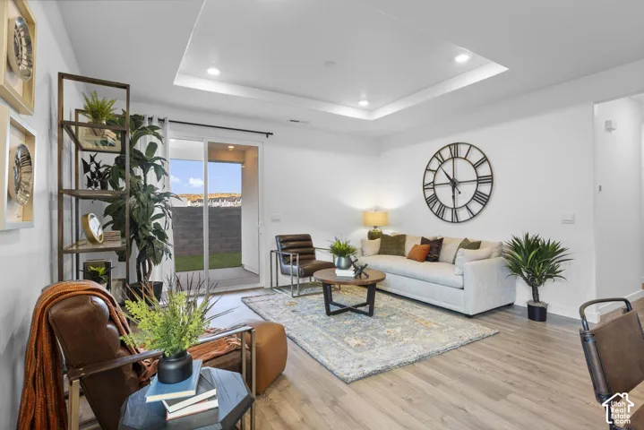 Tray ceiling with recessed lighting, wood-finish flooring, sliding glass door to outdoor patio, and a grass yard