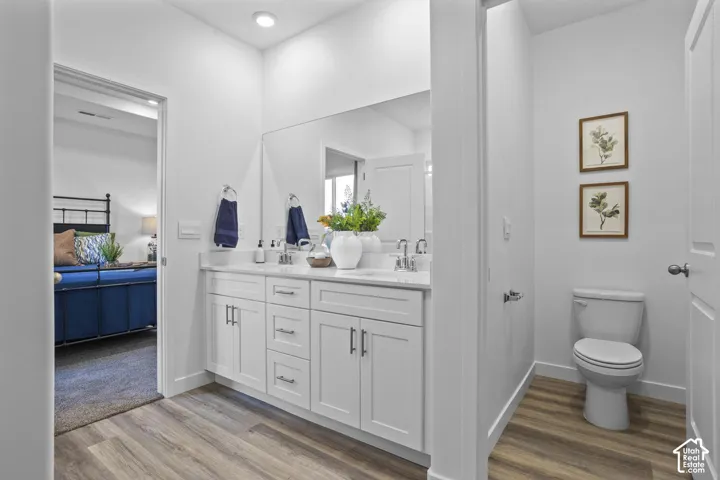 Dual vanity with white cabinetry, wood-finish flooring, recessed lighting, and a commode