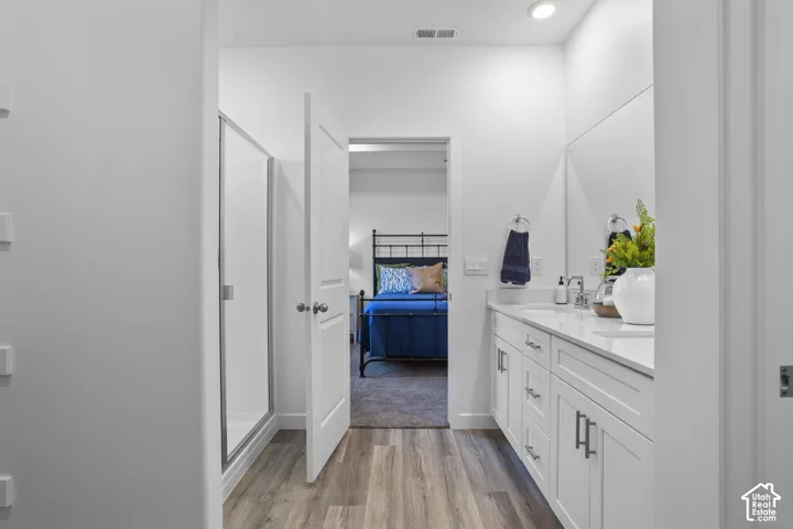 Bathroom featuring a glass-enclosed shower, wood-finish flooring, a double vanity with white cabinetry, a light-toned countertop, and an integrated mirror