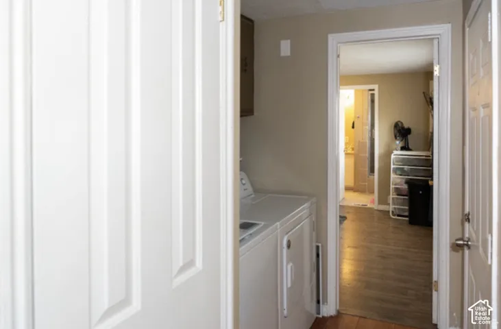 Laundry room featuring white cabinetry, a stacked washer/dryer unit, and wood-finish flooring that extends throughout the home