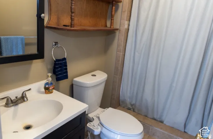 Bathroom featuring a vanity with an integrated sink, a framed mirror, a built-in toilet, a corner wall shelf, and tiled flooring