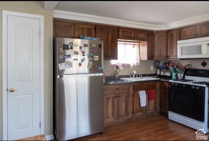 Wood-finish flooring complementing rich wood cabinetry, stainless steel refrigerator, white built-in microwave, and a black range
