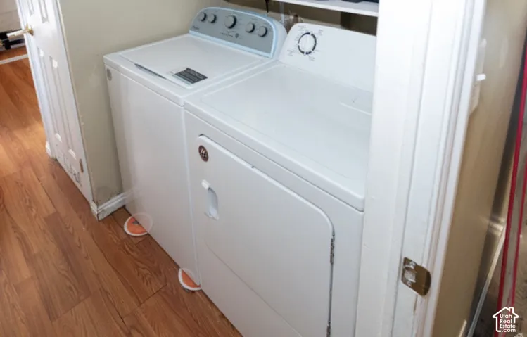 Laundry area featuring a stacked washer and dryer, wood-finish flooring, and white trim