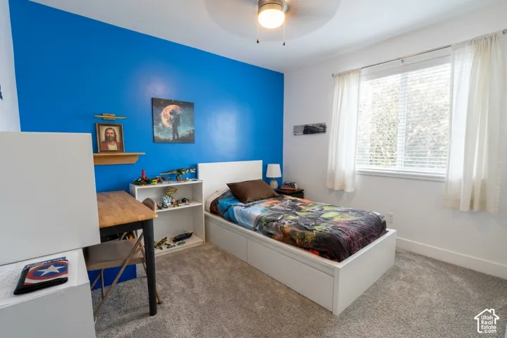 Carpeted room featuring a white-framed window with blinds, a built-in ceiling fan with lighting, and a white storage bed frame