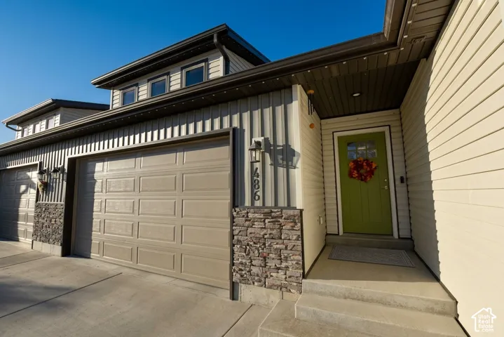 Exterior featuring a green entry door, concrete steps, and a two-car garage with paneling