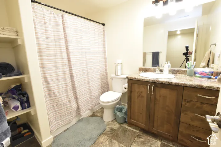 Bathroom featuring a dark wood-finish vanity with a single basin sink, a large mirror, built-in shelving, and tile flooring