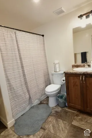 Shower with curtain rod, toilet, wood-finish vanity with countertop and integrated sink, wall-mounted mirror, and tiled flooring