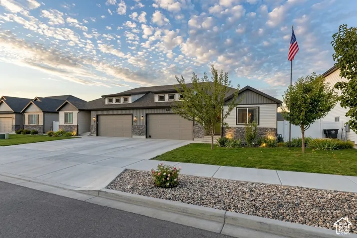 Modern exterior featuring horizontal siding and stone accents, concrete driveway, attached two-car garage, dormer windows, and established landscaping