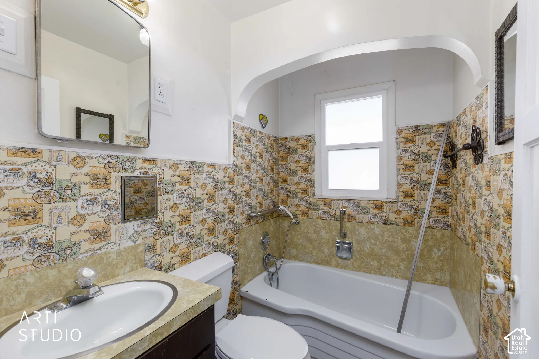 Vanity with integrated sink, wall-mounted mirror with overhead lighting, patterned wall tiling, and a built-in bathtub with an overhead window