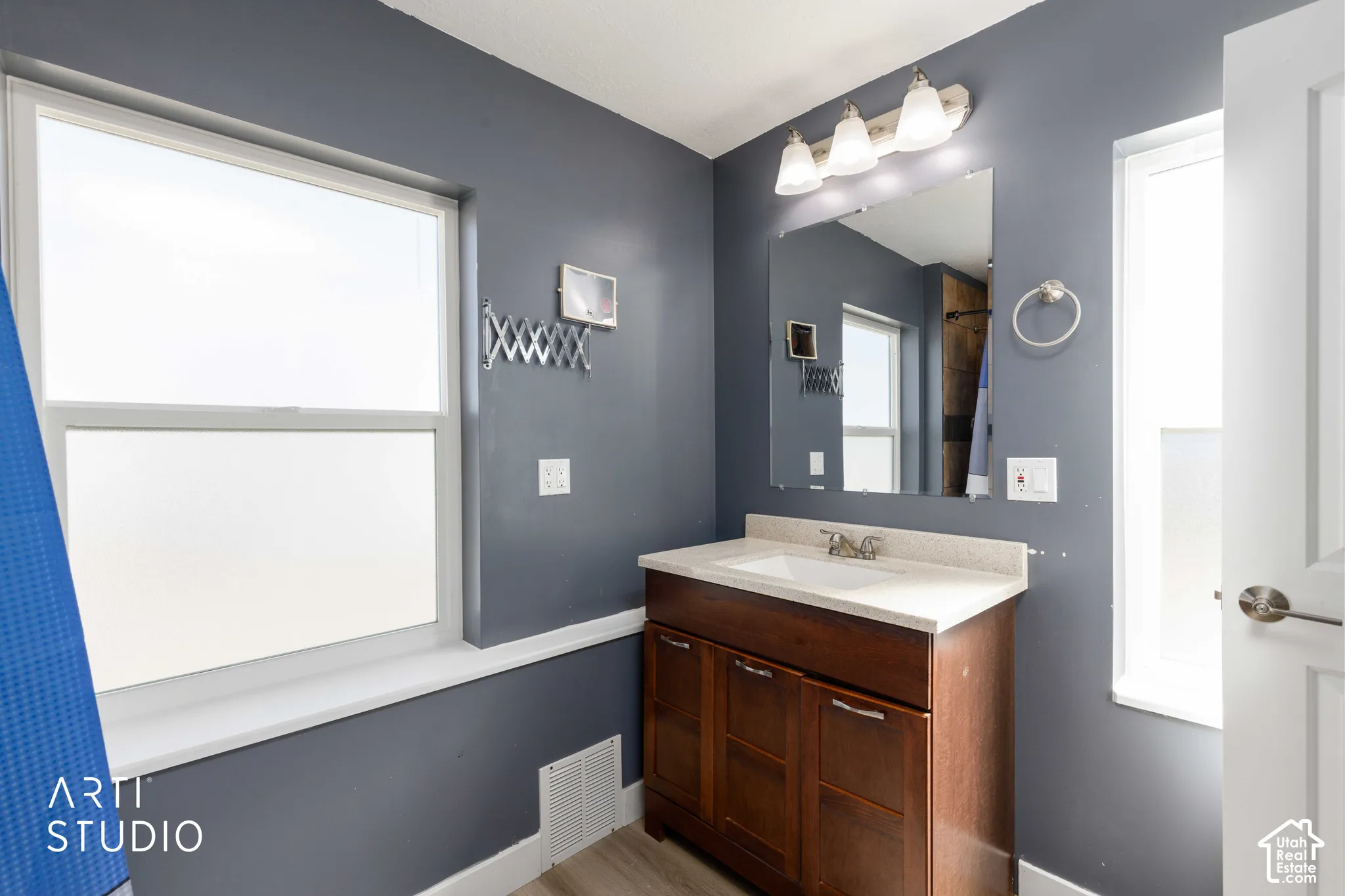 Wood-finish vanity with an integrated sink and light-toned countertop, complemented by a large wall mirror and overhead vanity lighting