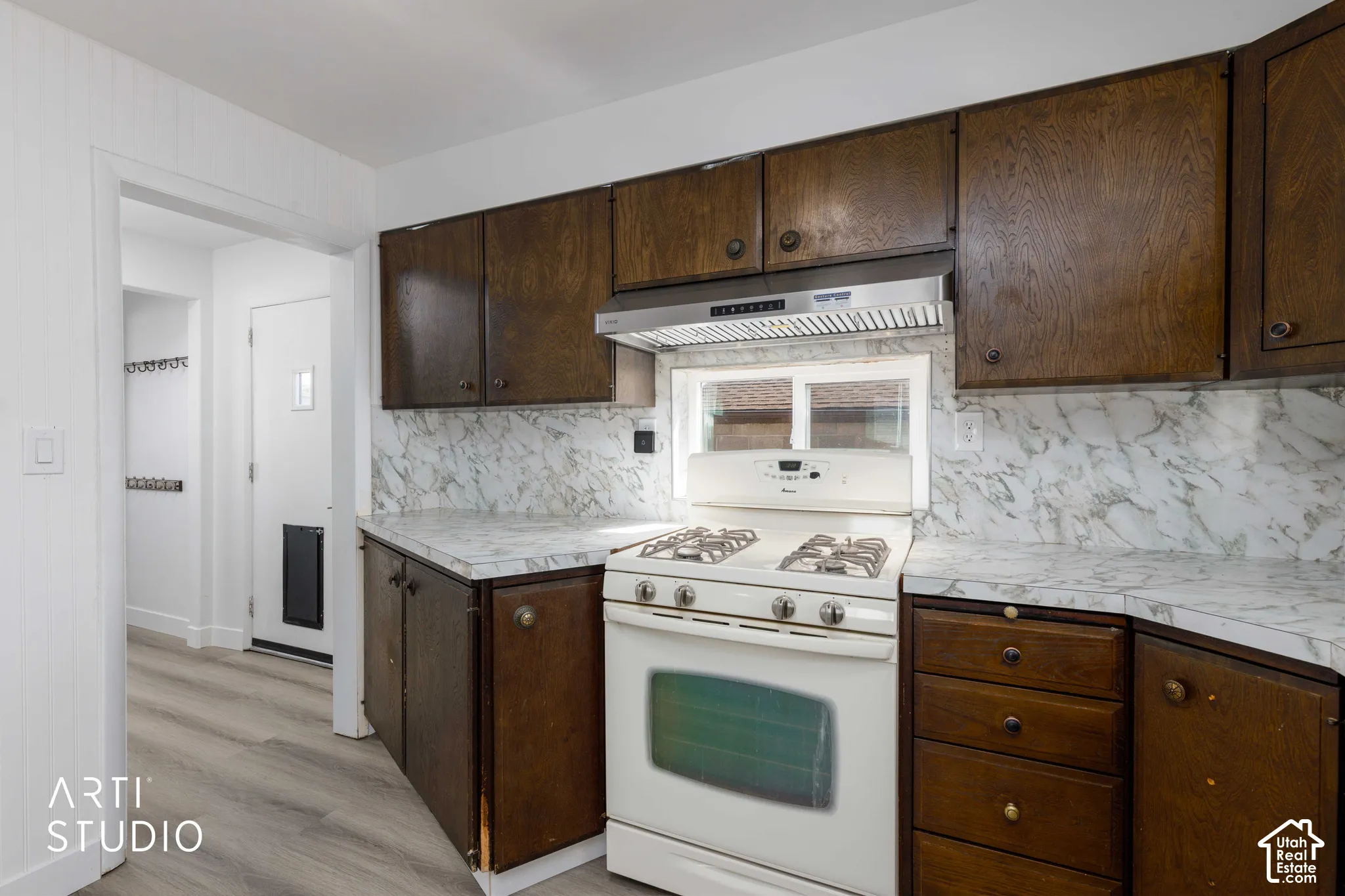 Wood-finish wall cabinetry, white appliance, marbled-finish countertops, and wood-finish flooring