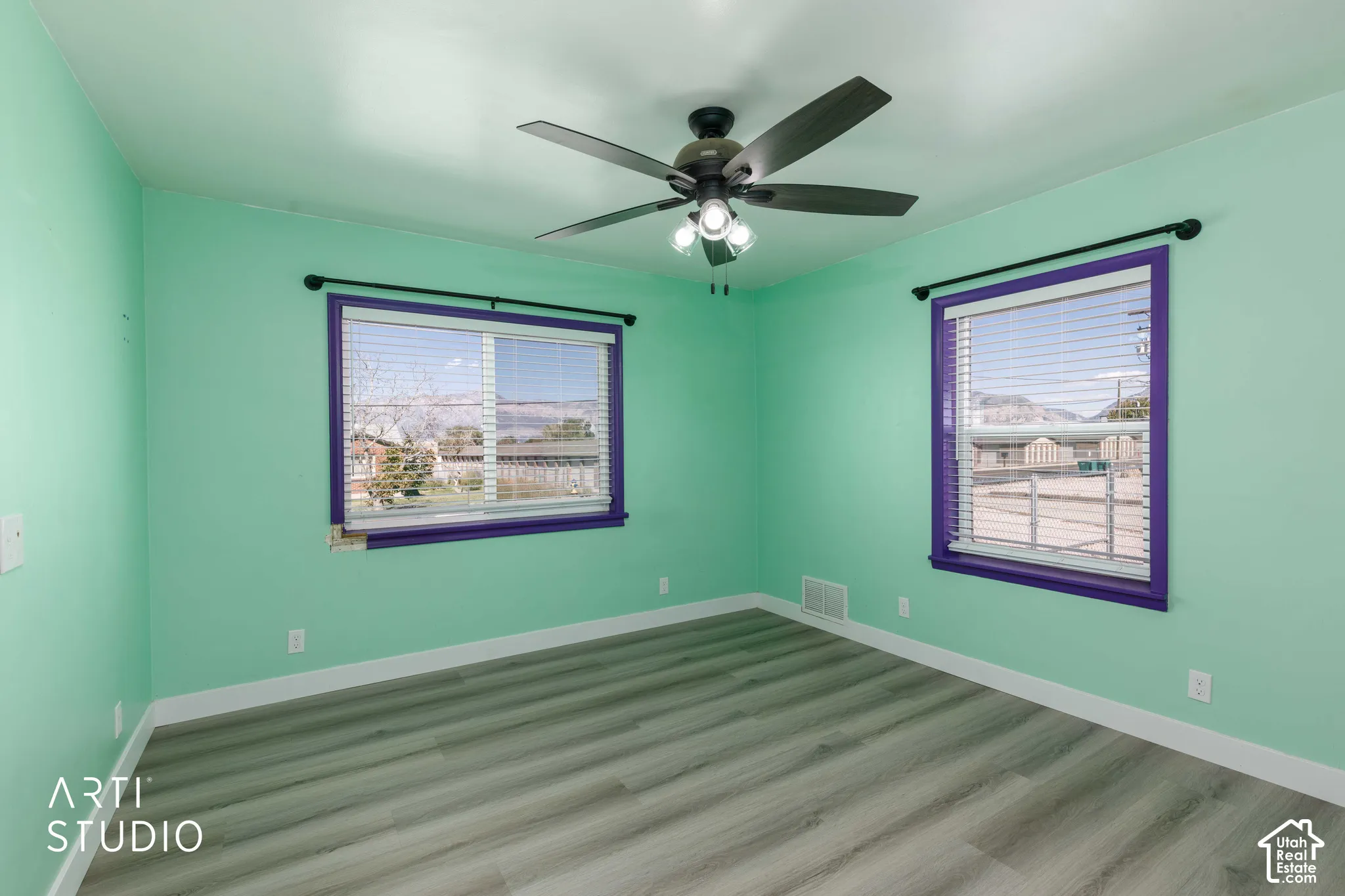 Wood-finish flooring, two windows with blinds, and a ceiling fan with integrated lighting