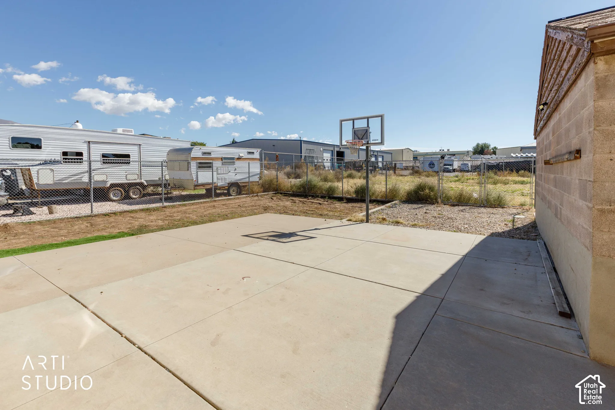 Concrete patio with a basketball hoop, chain-link fencing, and an adjacent brick structure