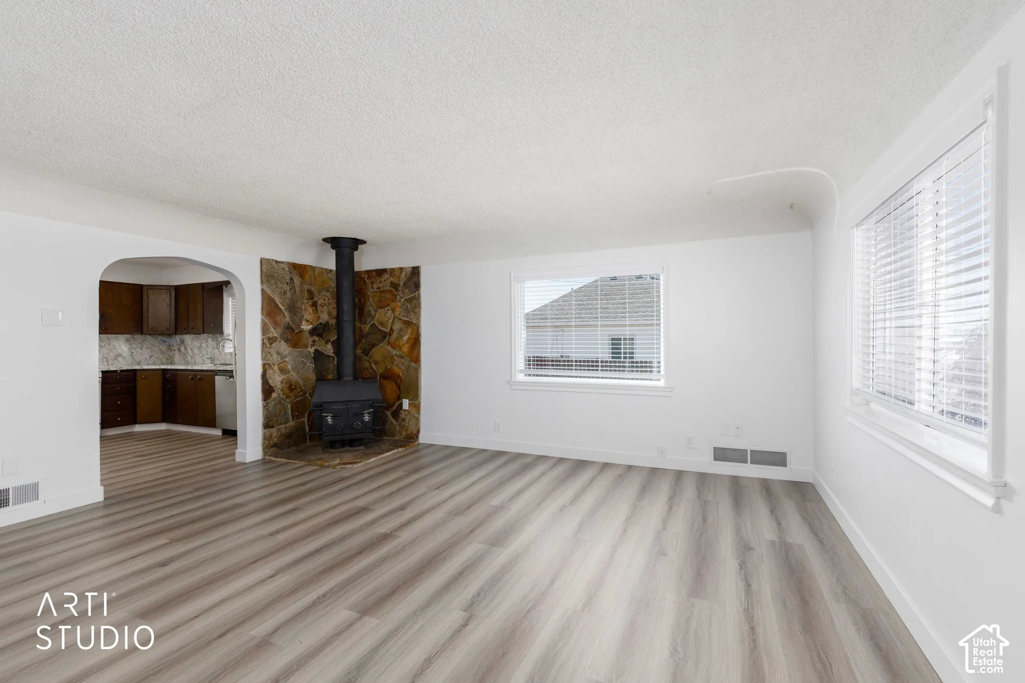 Wood-finish flooring throughout, multiple windows with blinds, and a stone-clad wood-burning stove