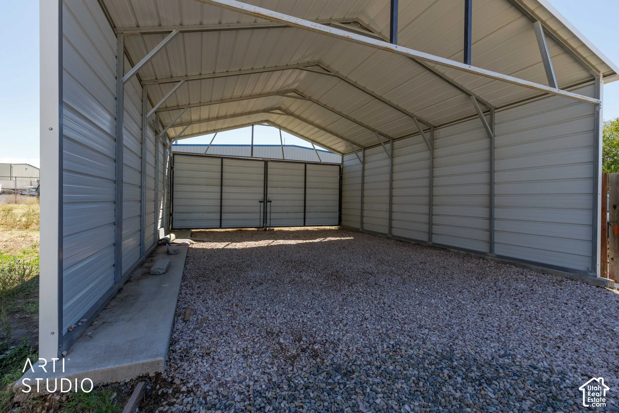 Metal carport structure with a gravel floor, concrete base, and an additional enclosed storage area