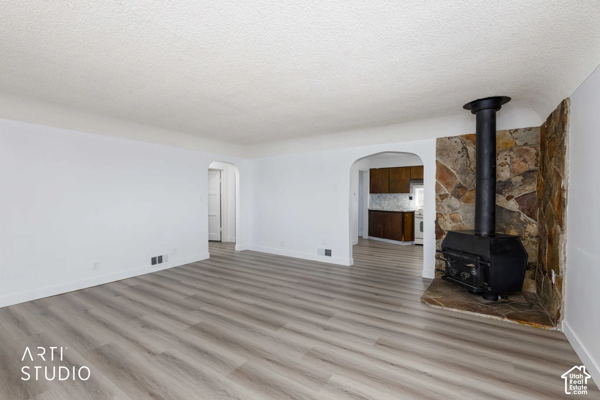 Spacious room featuring wood-finish flooring, a prominent stone accent wall, and a black wood-burning stove on a stone hearth