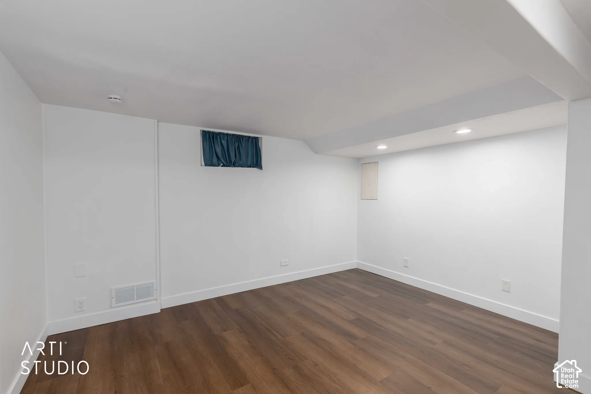 Recessed lighting illuminates the wood-finish flooring and bright white walls