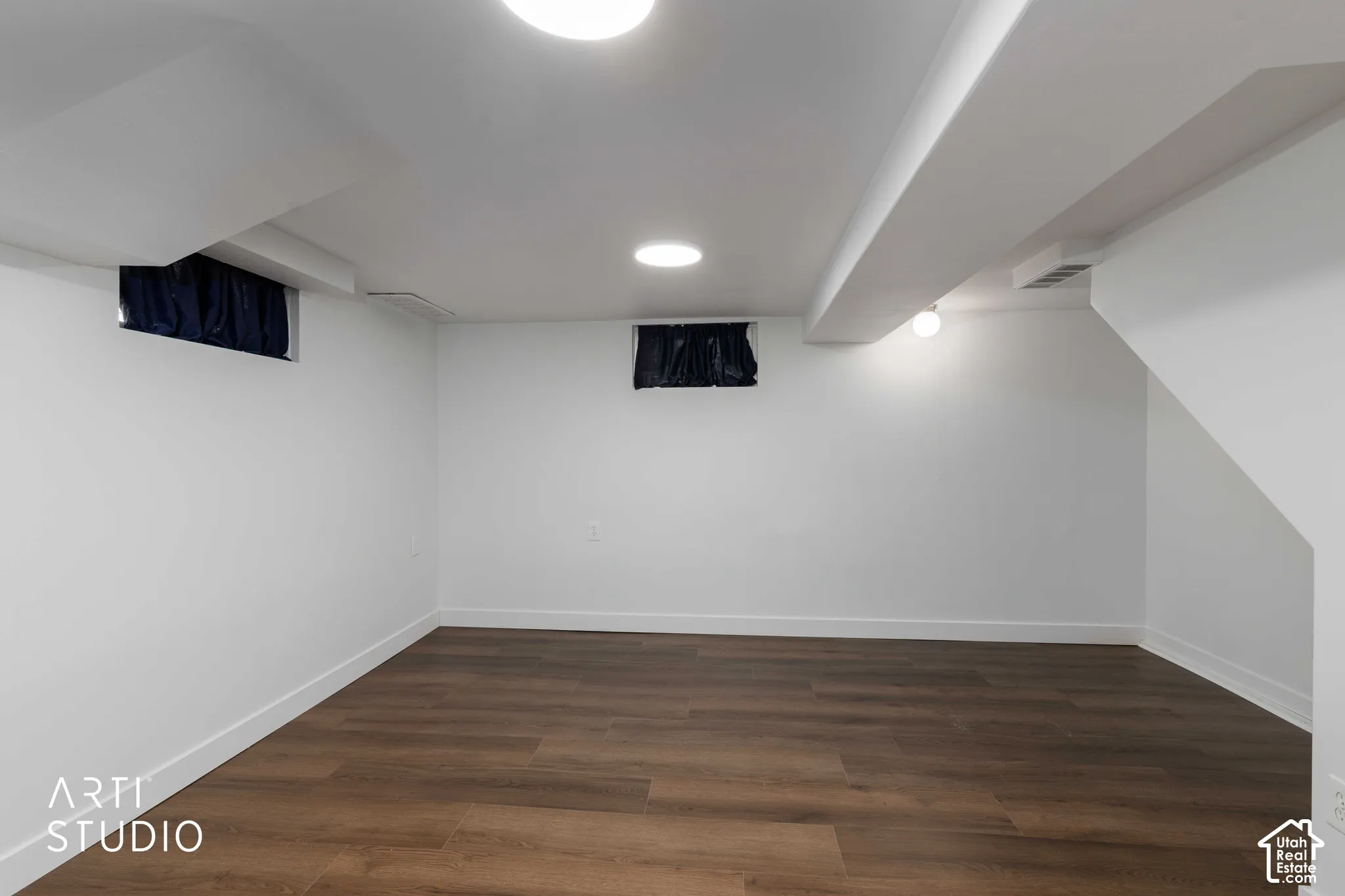 Smooth white walls, wood-finish flooring, recessed ceiling lighting, exposed ceiling beam, and painted staircase
