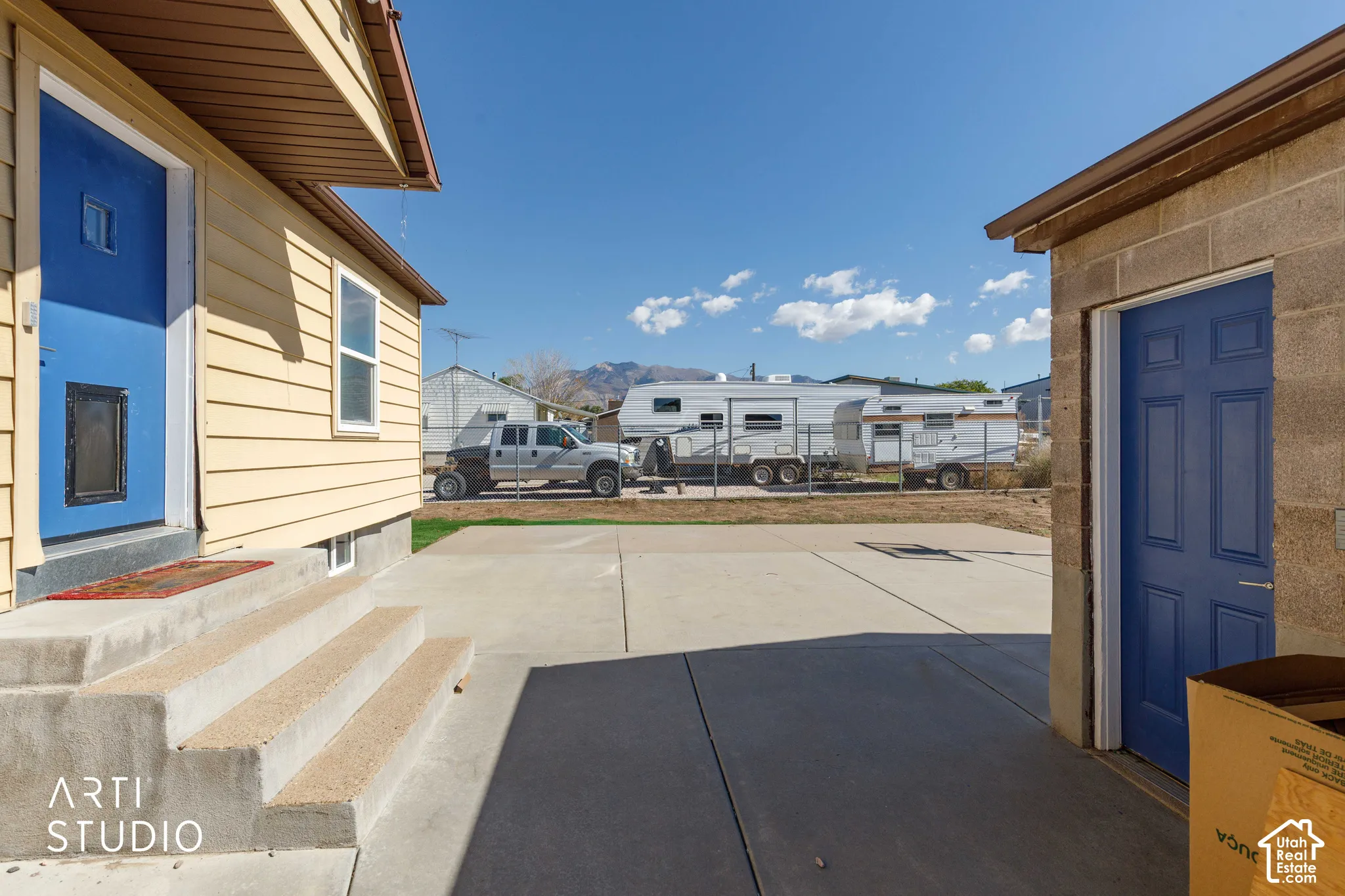 Concrete patio connecting two structures with blue doors and wood-look siding on the main building