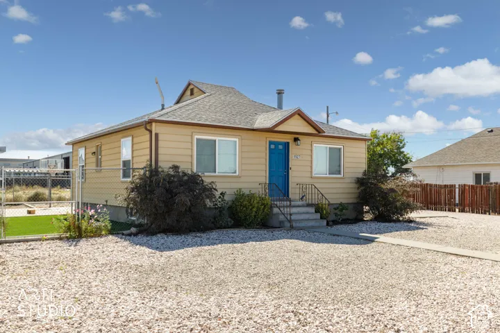 Single-story residence featuring light-colored siding, a blue entry door, and a gravel driveway