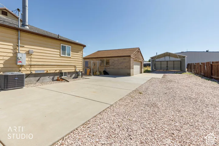 Concrete driveway, detached garage, metal carport, gravel lot, and wood fencing