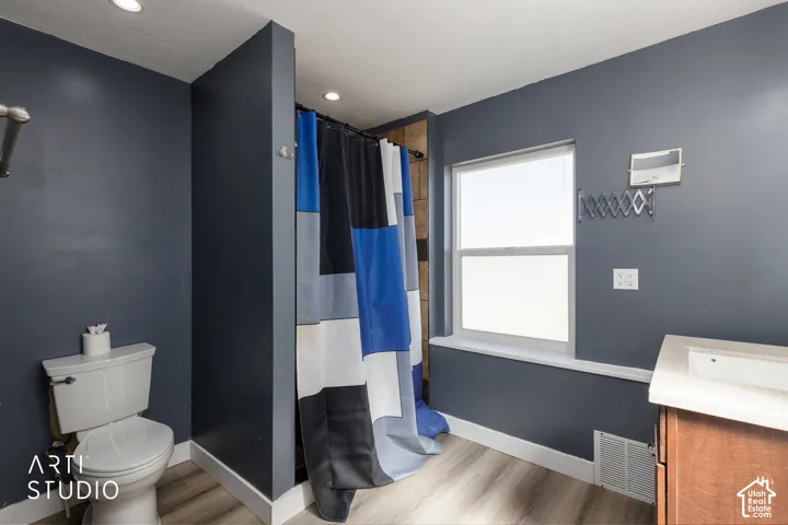 Modern bathroom featuring wood-finish flooring, a single window, recessed lighting, and a vanity with an integrated sink