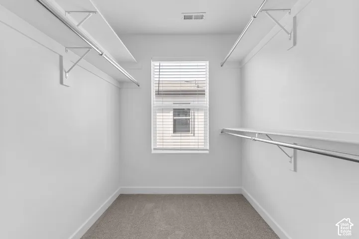 Built-in shelving and hanging rods, window with horizontal blinds, neutral carpet flooring, white painted walls
