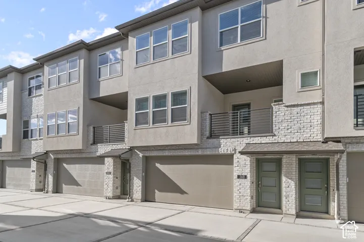 Contemporary multi-story exterior with stucco and stone veneer, multiple windows, covered entrance, and an integrated garage