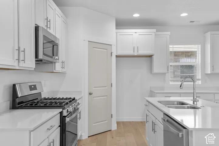 White shaker cabinetry, stainless steel appliances, light wood-finish flooring, white countertops, and an island with an undermount sink