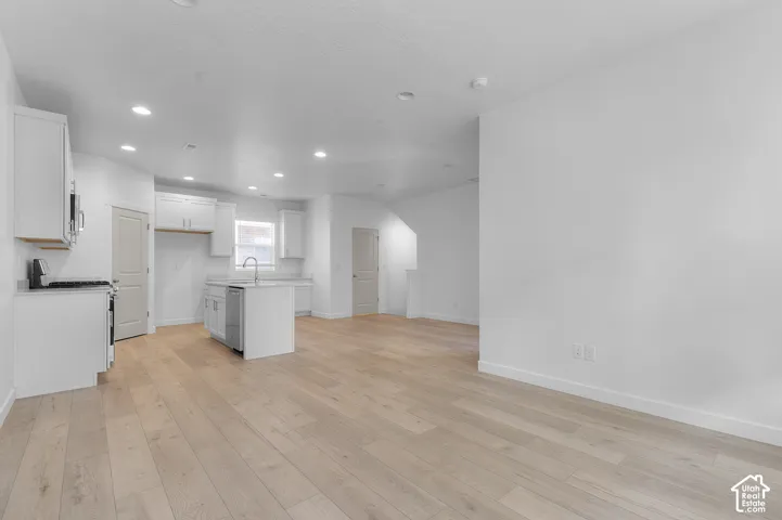 Open-concept kitchen featuring white cabinetry, a central island with a stainless steel sink, and wood-finish flooring