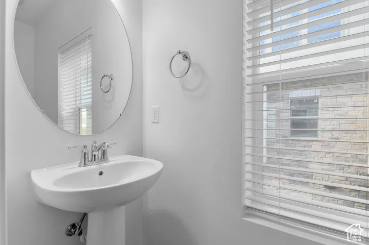 Pedestal sink with chrome faucet, circular wall mirror, and window with blinds