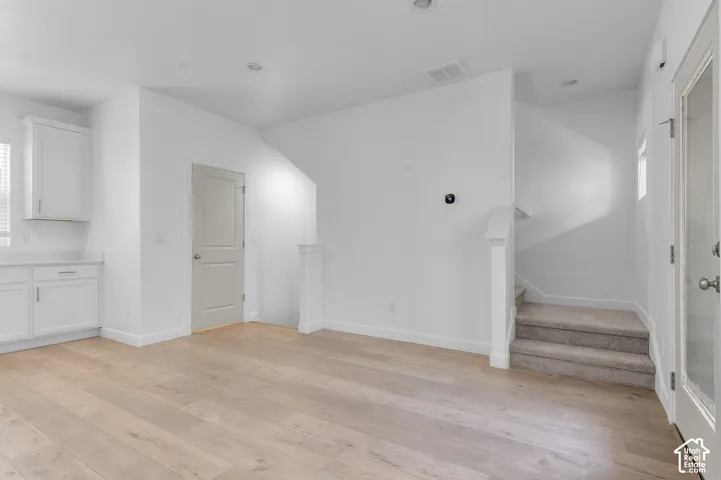 Wood-finish flooring, recessed lighting, white cabinetry, light countertops, and a carpeted staircase