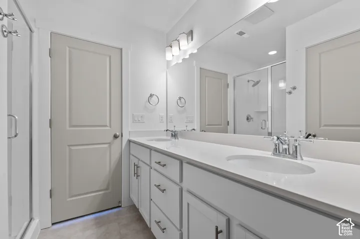 Double vanity with white cabinetry, polished chrome fixtures, and a glass-enclosed shower