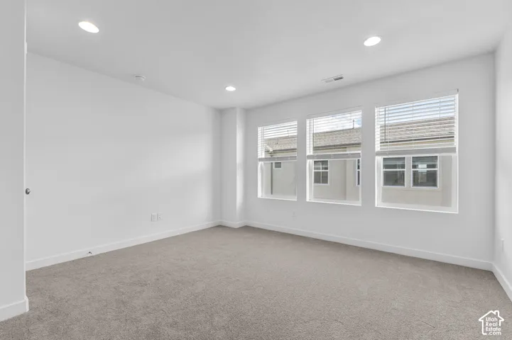 Three large windows with blinds, recessed ceiling lighting, and light-colored carpeting