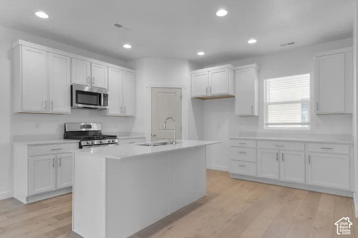 Kitchen featuring white cabinetry, stainless steel appliances, a center island with sink, light-toned wood-finish flooring, and recessed lighting