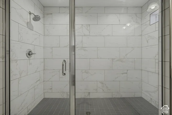 Walk-in shower featuring glass enclosure, white marble-look subway tile walls, gray tile flooring, and polished chrome fixtures