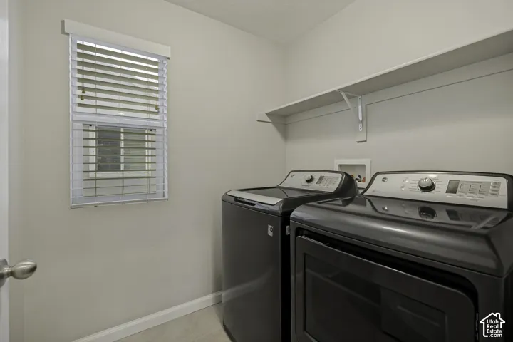 Functional laundry room featuring a window with blinds, a wall-mounted shelving unit, and plumbing connections for appliances