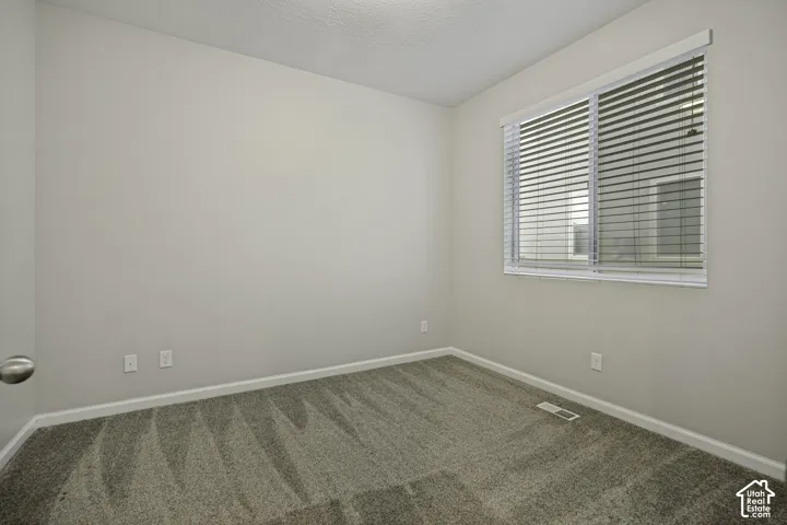 Neutral gray wall paint, textured ceiling, gray patterned carpeting, window with horizontal blinds, white trim