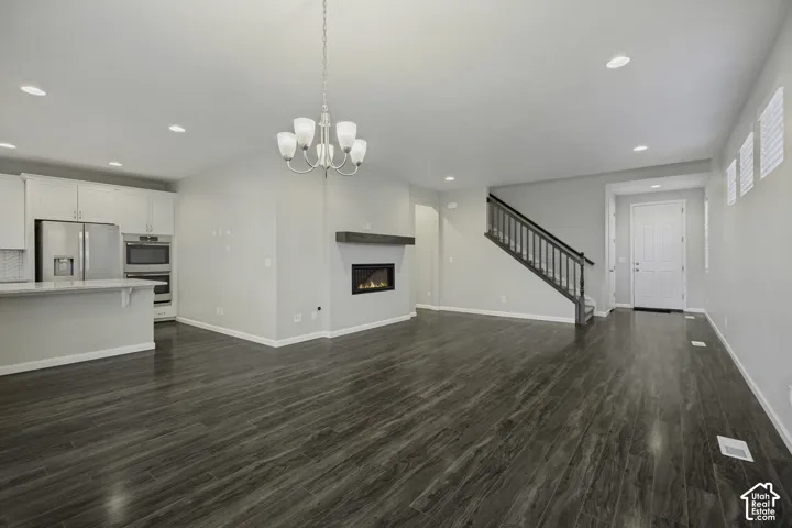 Open-concept living area featuring wood-finish flooring, a built-in fireplace with a mantel, a kitchen island with seating, stainless steel appliances, and a staircase with dark wood railings